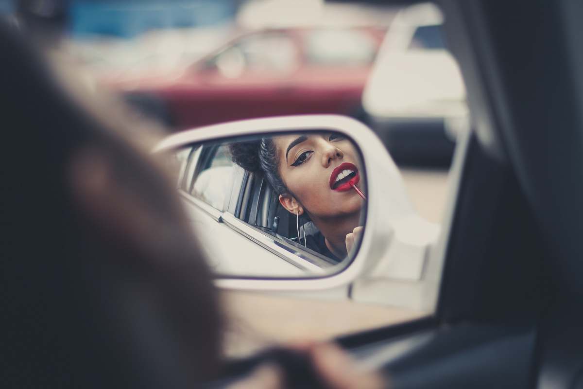 car mirror woman putting liquid lipstick on her lips while looking at vehicle's mirror during daytime female